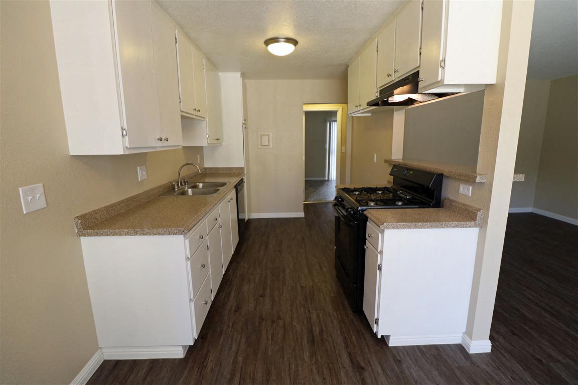 A kitchen with white cabinets and brown floors.